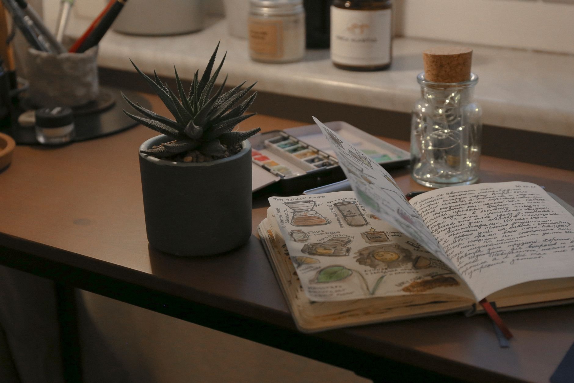 A warm, creative desk setup featuring a sketchbook, succulent, and artistic supplies.