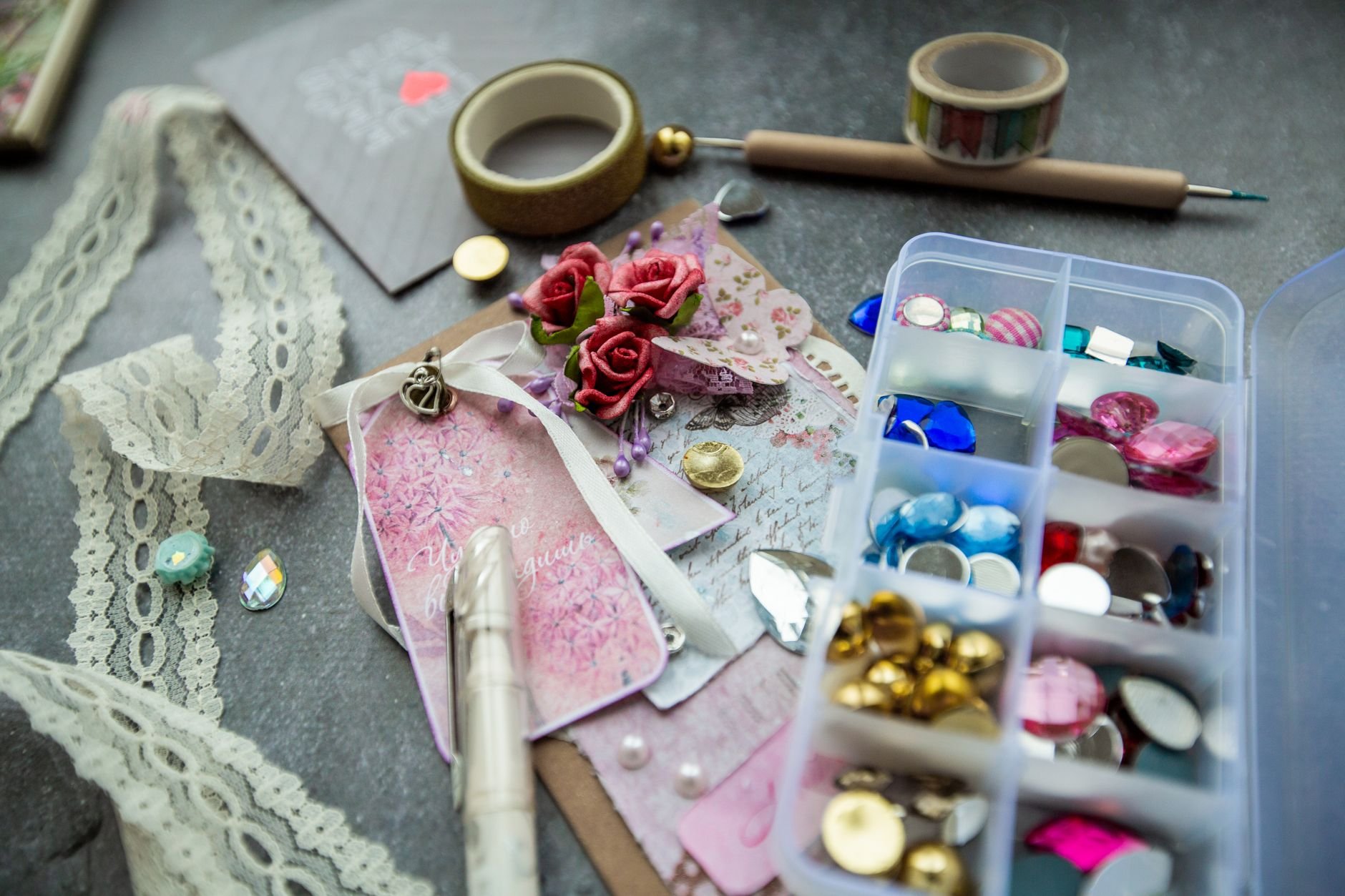 Colourful craft materials including decorative stones, lace, tape, and a handmade greeting card with flowers.